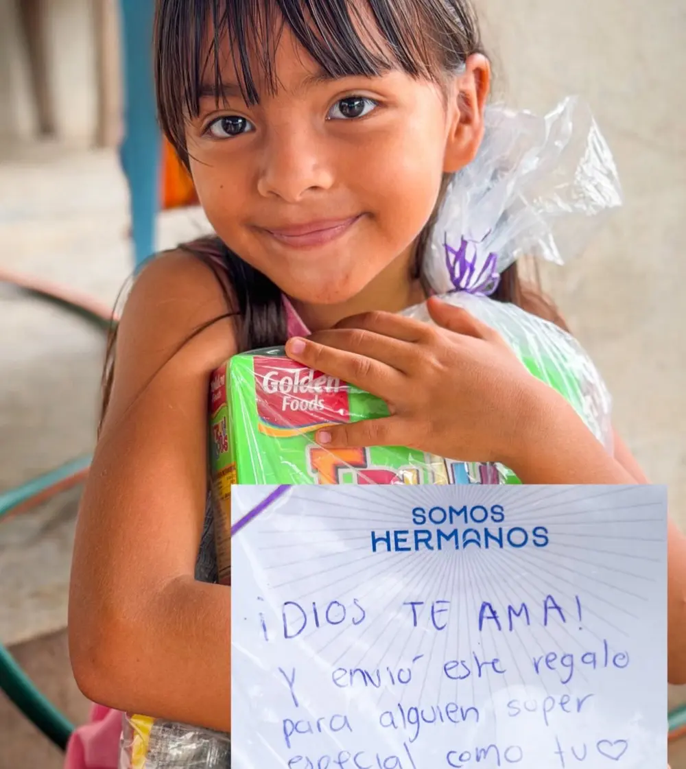 Niña sosteniendo una canasta con una carta que dice Dios te ama
