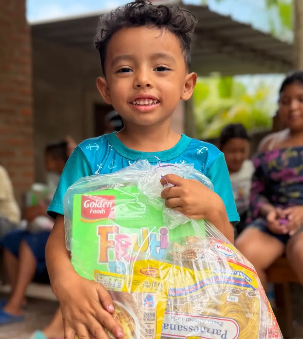 Niño con camiseta turquesa sonriendo con su canasta de ayuda de Somos Hermanos